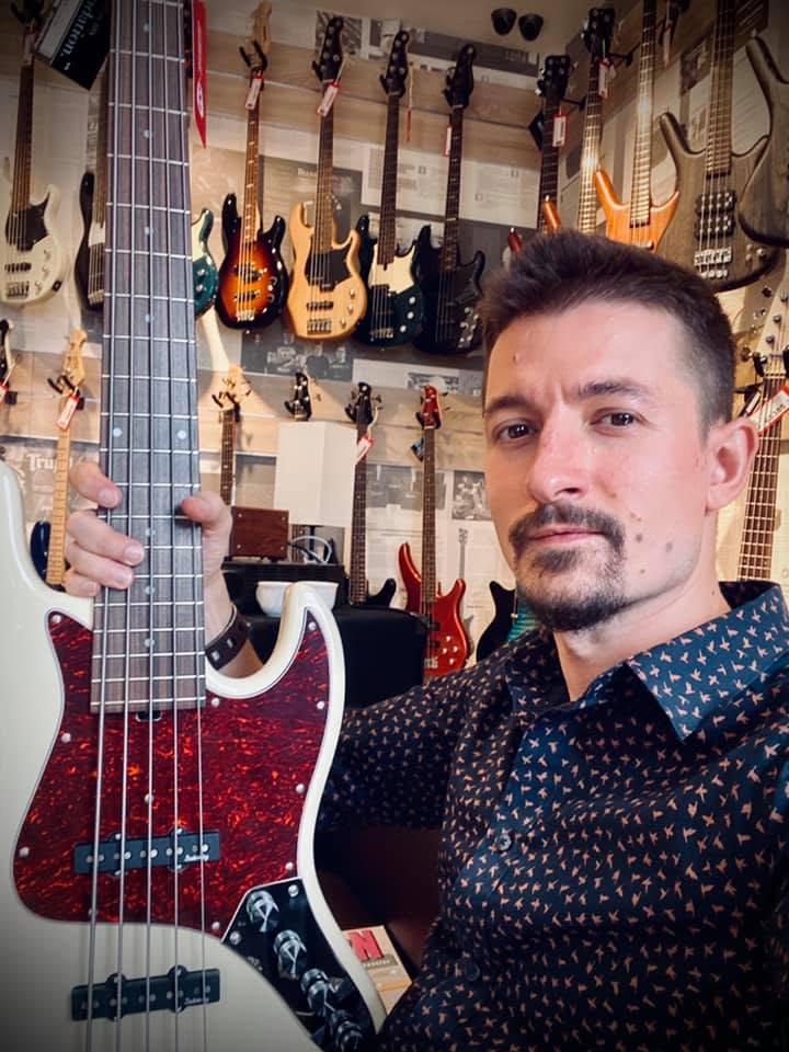 Igor Odaryuk holding a white jazz bass with a tortoise pickguard in a bass shop